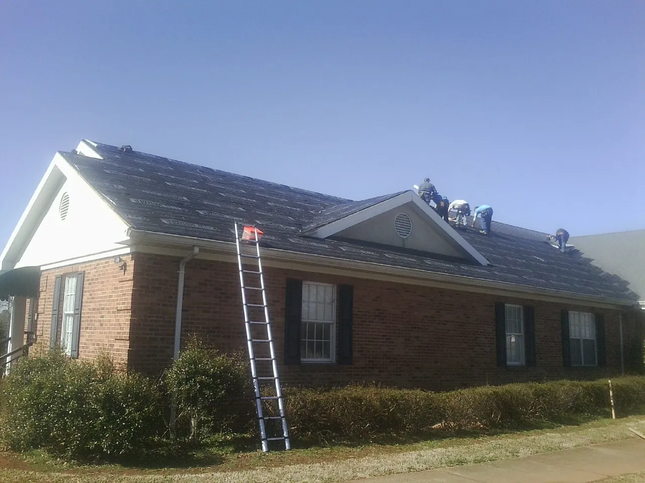 Crew tearing shingles off a brick ranch roof with a ladder set — Emergency Roof Repair work by our crew in Zeeland