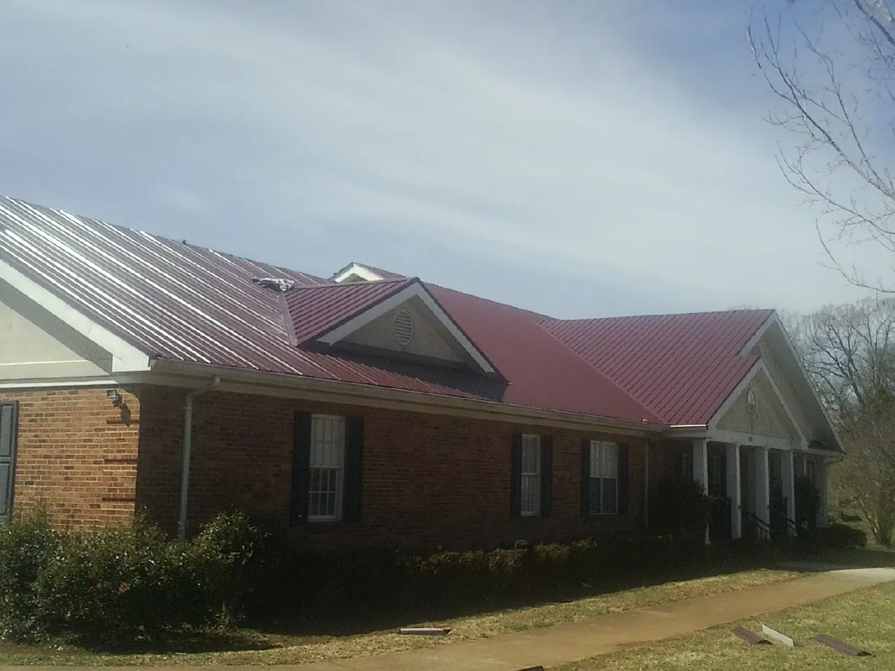 Red metal roof with gabled entries on a long brick building, from a Hail Damage Roof Repair job in Zeeland