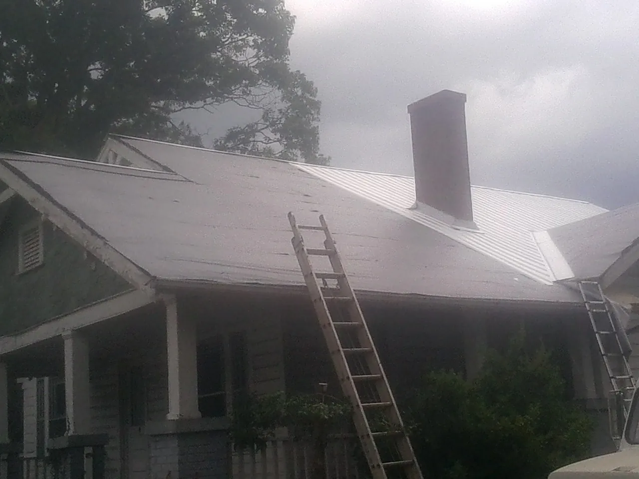 Ladders against a metal roof on an older home with a brick chimney in Zeeland