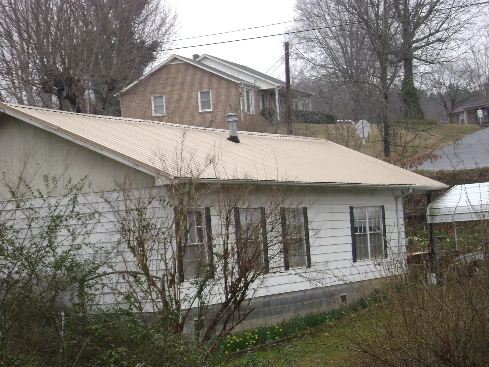 Tan metal roof on a white sided house set into a hillside — Commercial Roofing by Roofing Brothers in Zeeland