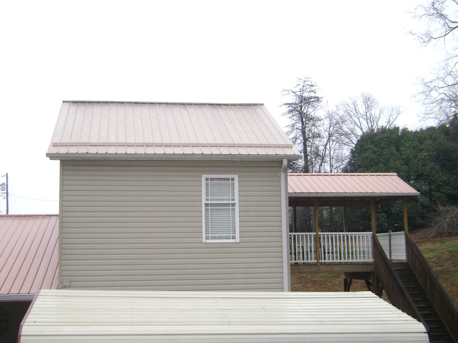 Tan metal roofs on a two story addition and attached porch, from a Roof Replacement job in Zeeland